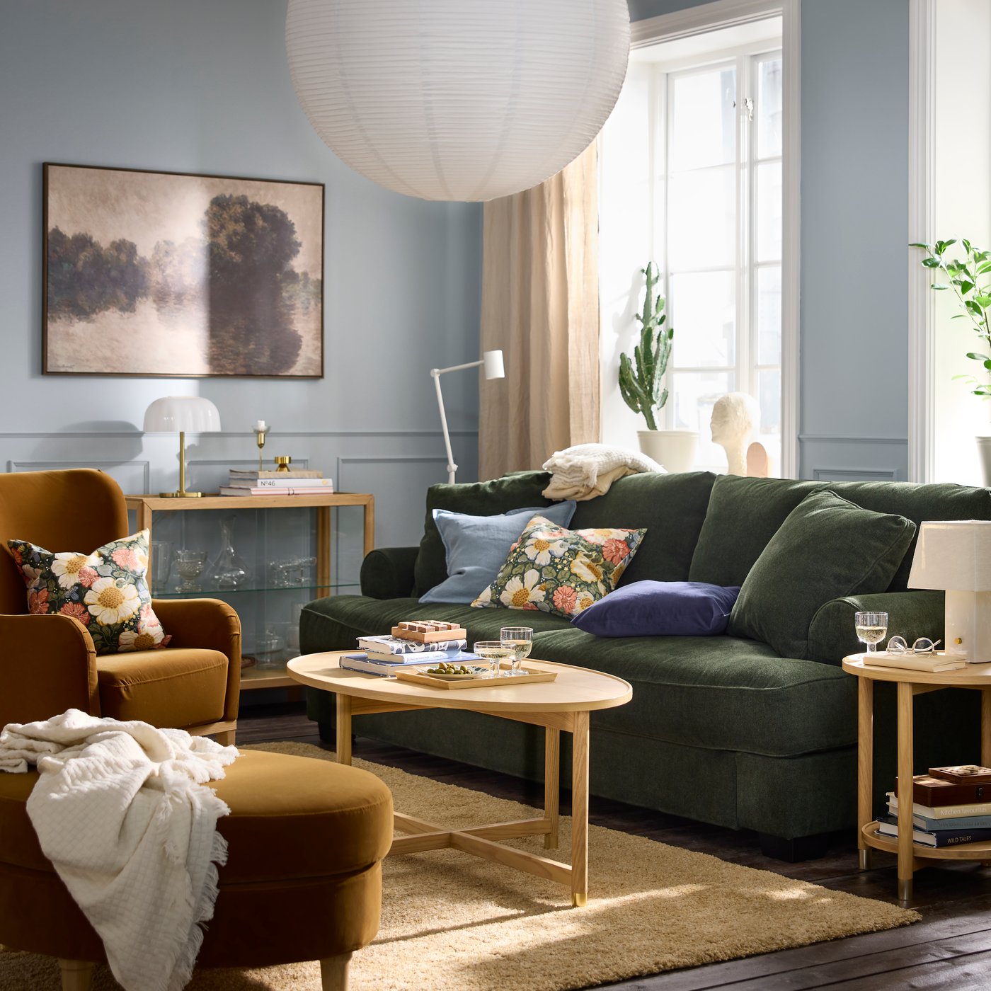Ein farbenfrohes Wohnzimmer im sanften Sonnenlicht mit einem VALNÄS Sofa, Kissen mit Blumenmuster, einem VALNÄS Fußhocker und einem Couchtisch.