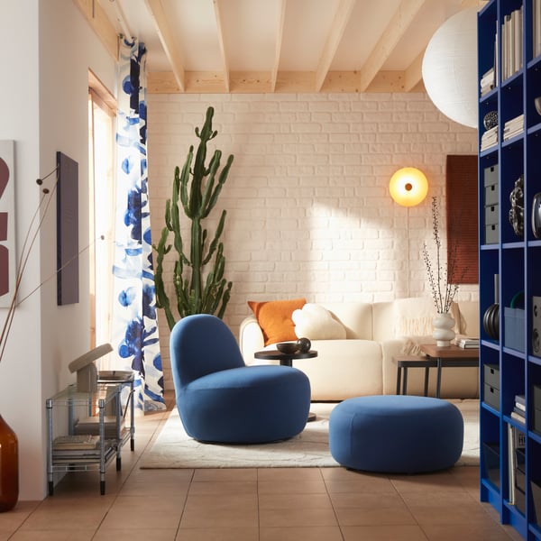 A living room with a Gunnared dark blue LILLESÄTER swivel easy chair in soft fabric beside an off-white sofa and green plants.