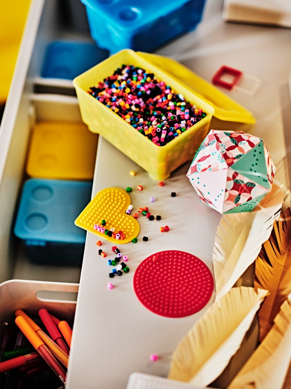 An open yellow/blue GLIS box with lid filled with mixed colours PYSSLA beads on a DUNDRA activity table with storage.