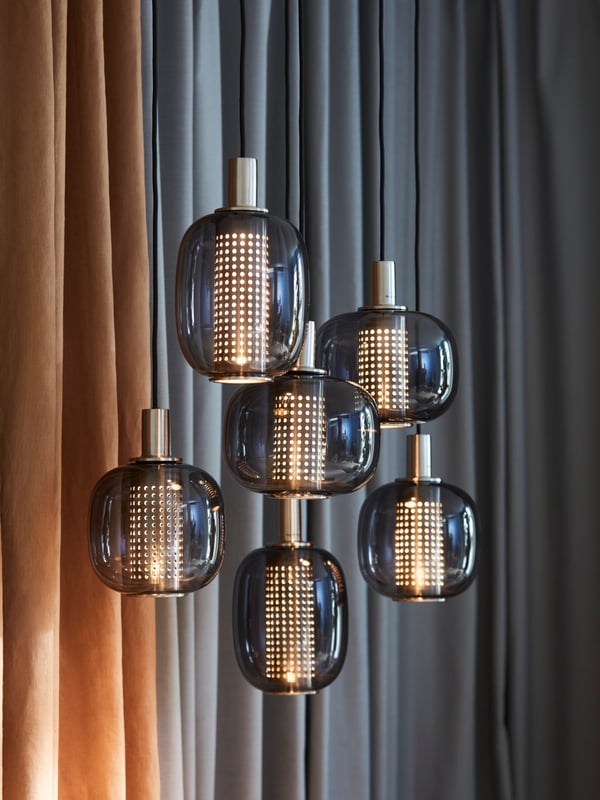Two HÖGVIND pendants with three lamps form a cluster of six bulbs in front of dark-beige DYTÅG and grey GUNNLAUG curtains.