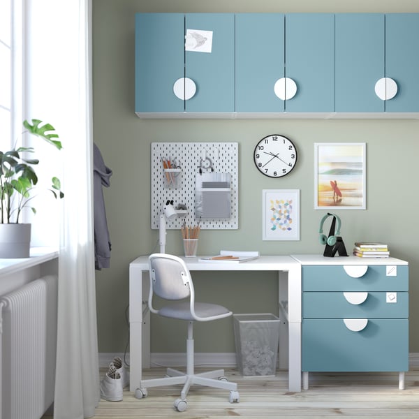 Child's bedroom with a study table next to a blue SMASTAD drawer system and blue SMASTAD cabinets mounted on the wall above the table area. 