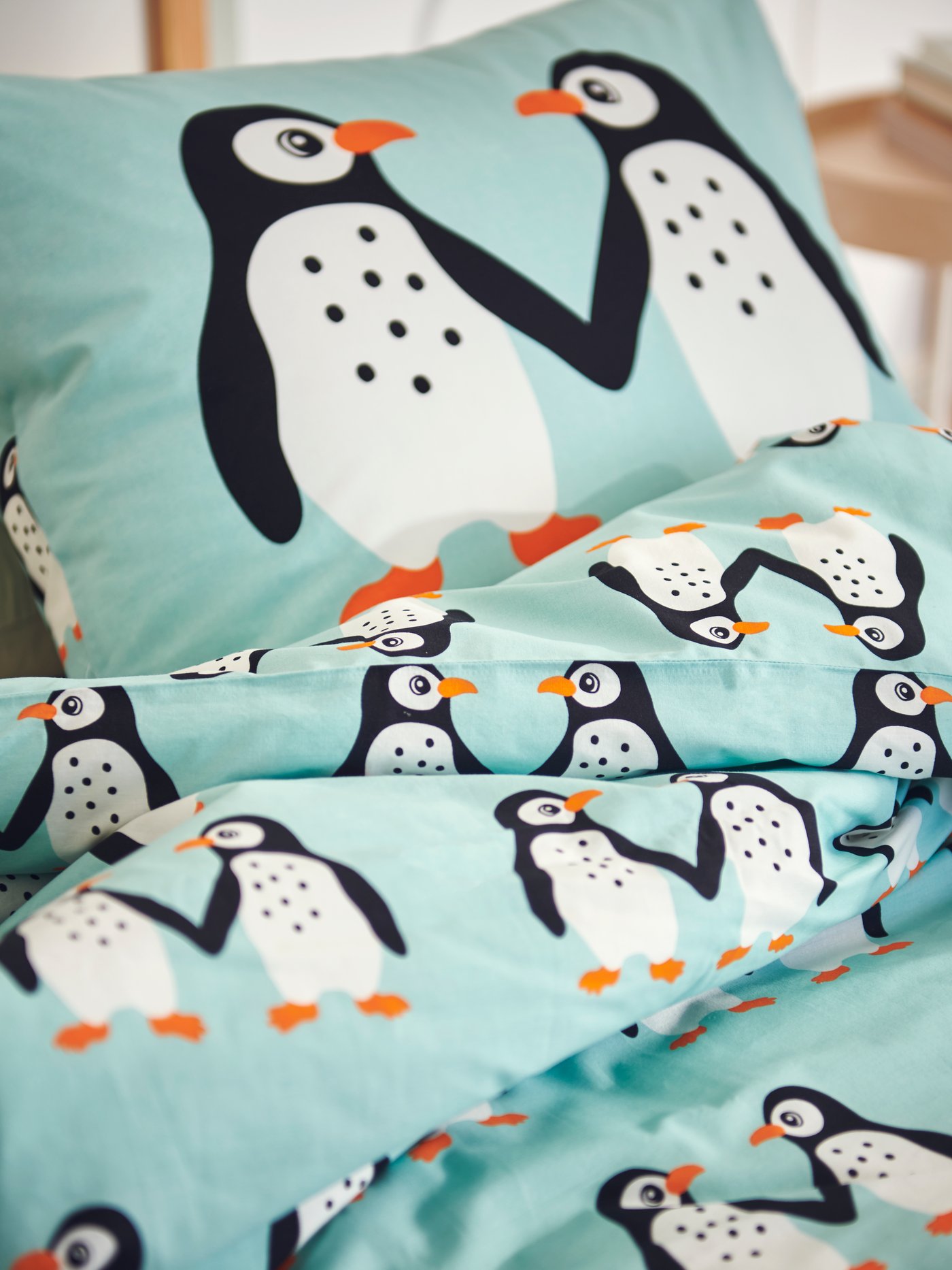 A pillow and a duvet for a child in a BLÅVINGAD pillowcase and duvet cover with a penguin pattern lie on a bed.