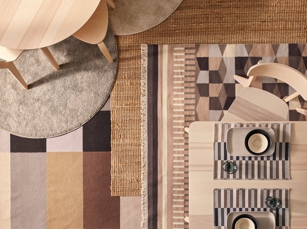 Two ash veneer LISABO tables and chairs stand on a floor with different rugs, including a LOHALS rug and some patterned ones.