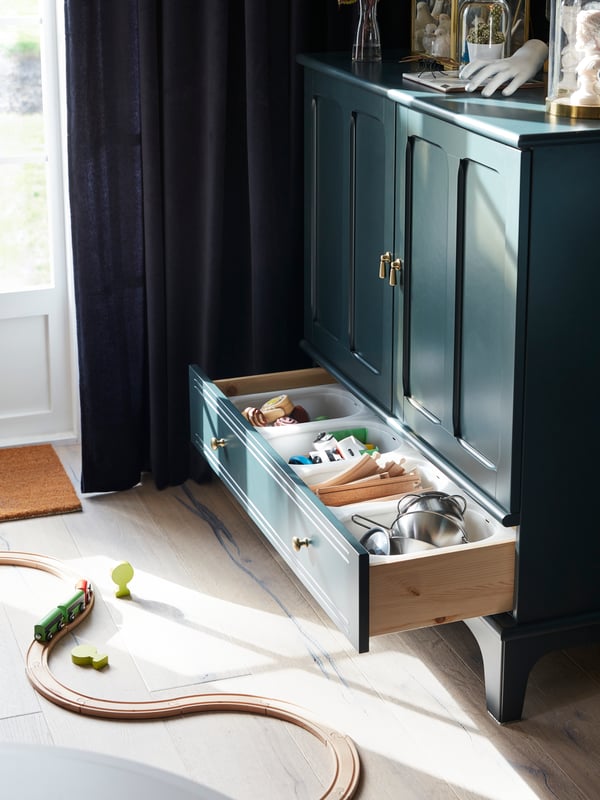 The bottom drawer of a LOMMARP cabinet is open. Children’s toys are stored inside, and there’s a train set on the floor.