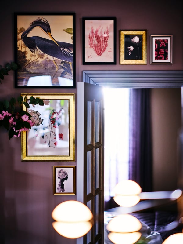 Art framed in black FISKBO frames and SILVERHÖJDEN frames in silver and gold above and next to an open door.