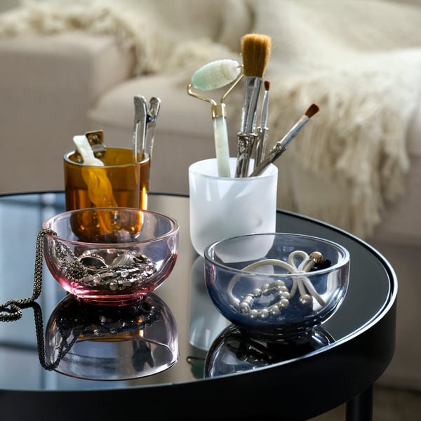 Two TALLTITA tealight holders separated to form four individual parts set on a side table and filled with beauty accessories.