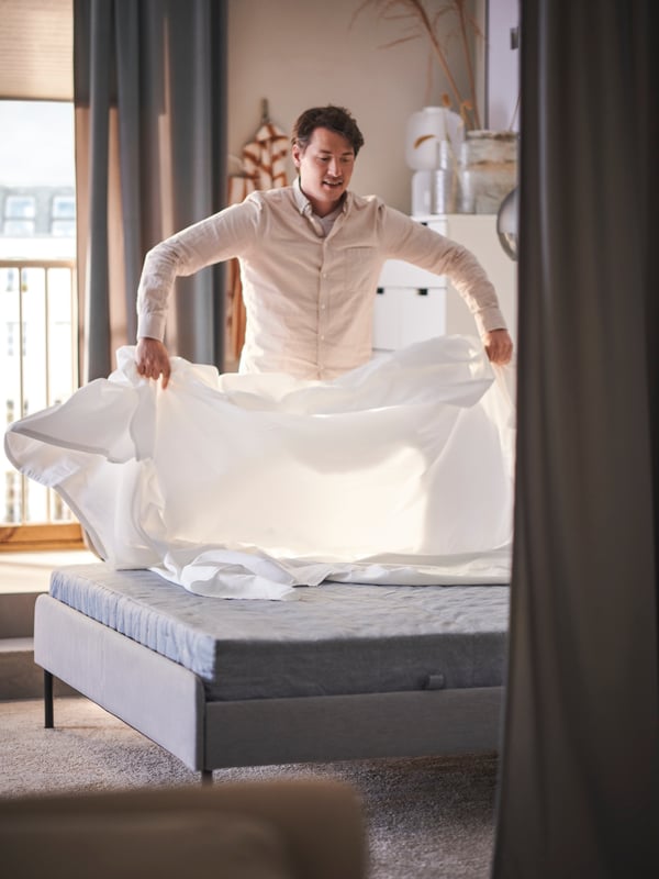 Un hombre haciendo la cama con una sábana blanca DVALA.