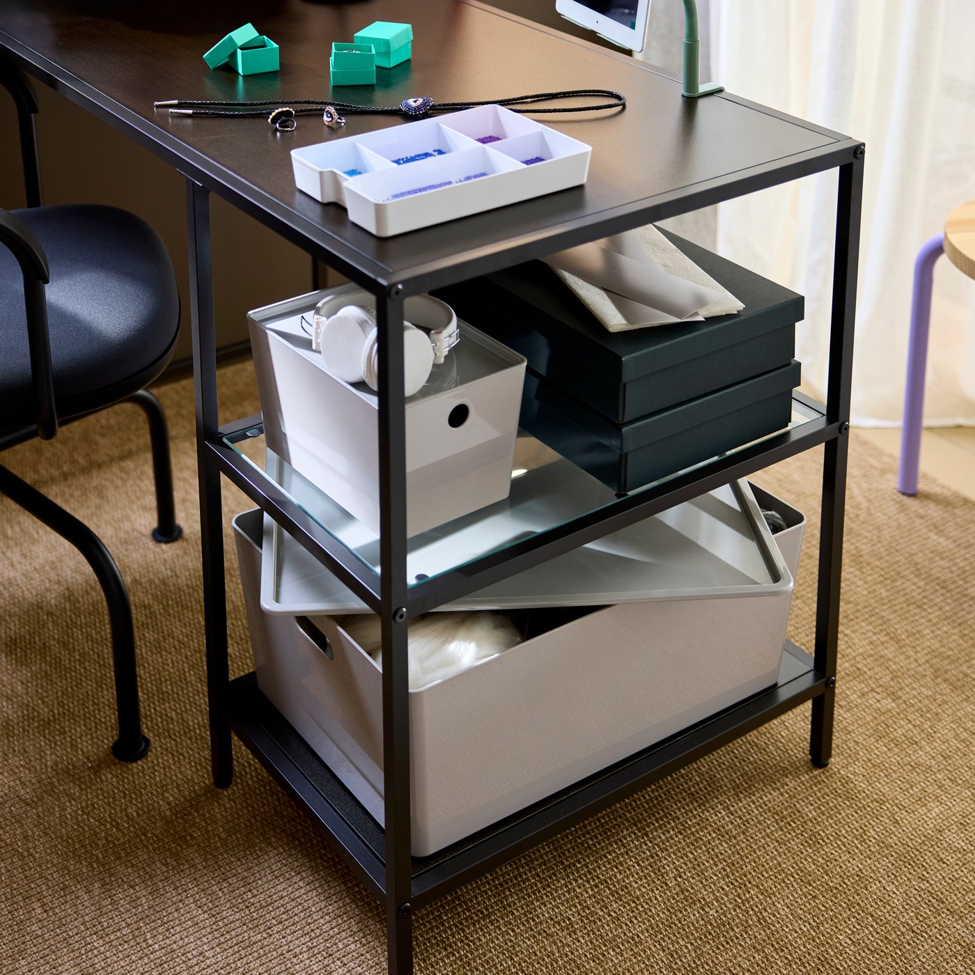 A close-up on a workspace setup with a black-brown VITTSJÖ desk with glass shelves, storing boxes and crafting supplies.