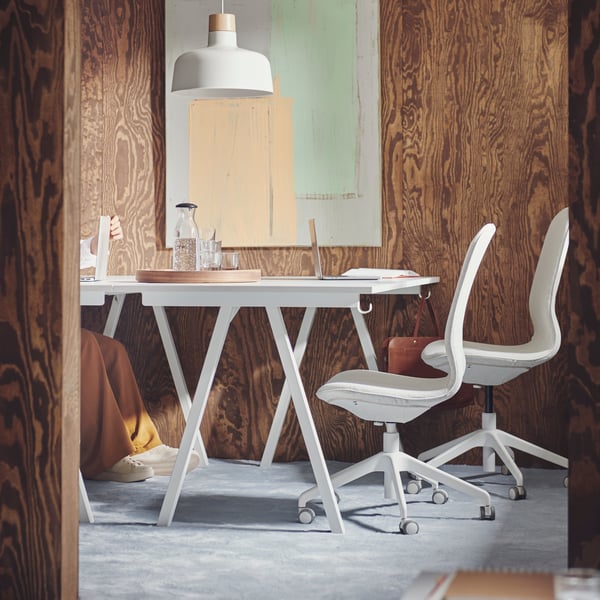 A carpeted, brown, wood-panel conference space with white TROTTEN desks and two beige-and-white LÅNGFJÄLL conference chairs.