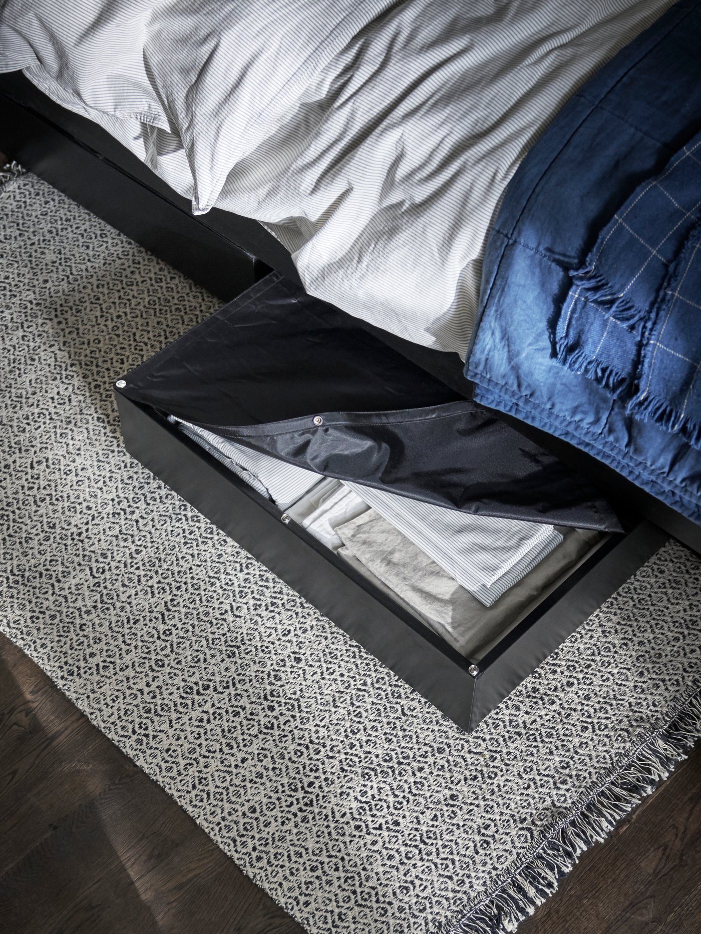 Gray underbed storage box partially sticking out from under bed with sheets in it