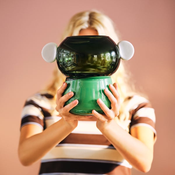 Person holding a green sculptural IKEA PS 2026 glass vase with playful ear-like details.