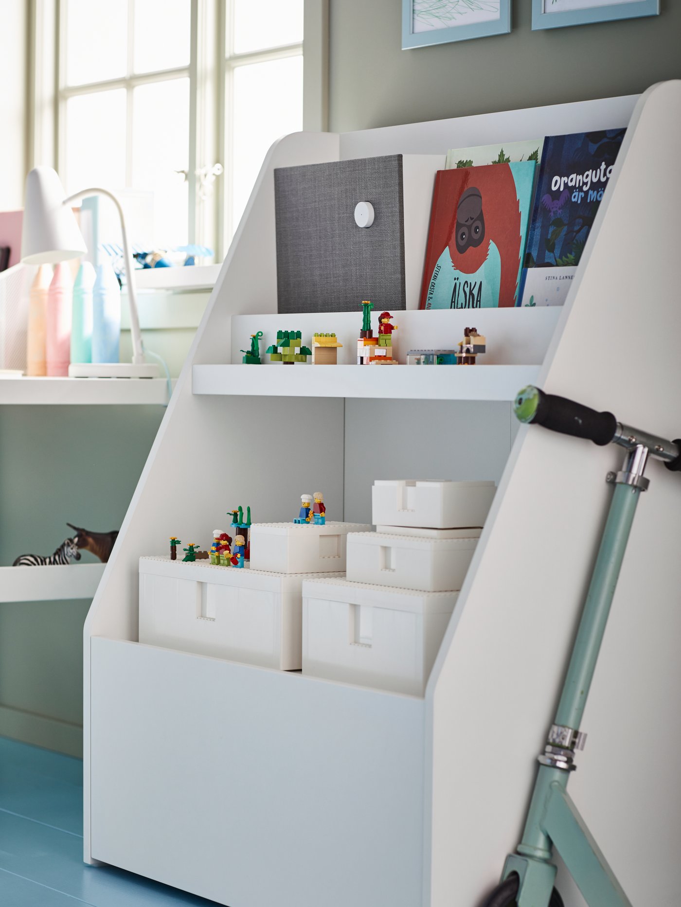 A book display holding books, a Bluetooth® speaker and several white BYGGLEK LEGO® boxes with lids and building blocks.