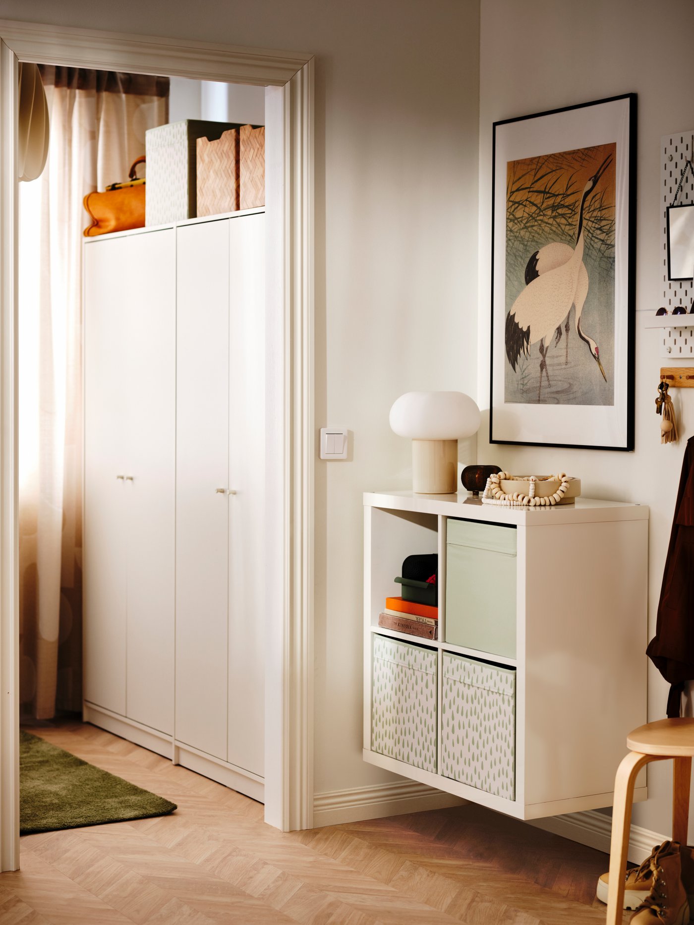 A white KALLAX storage unit with boxes inside has been mounted to the wall of a minimalist hallway.