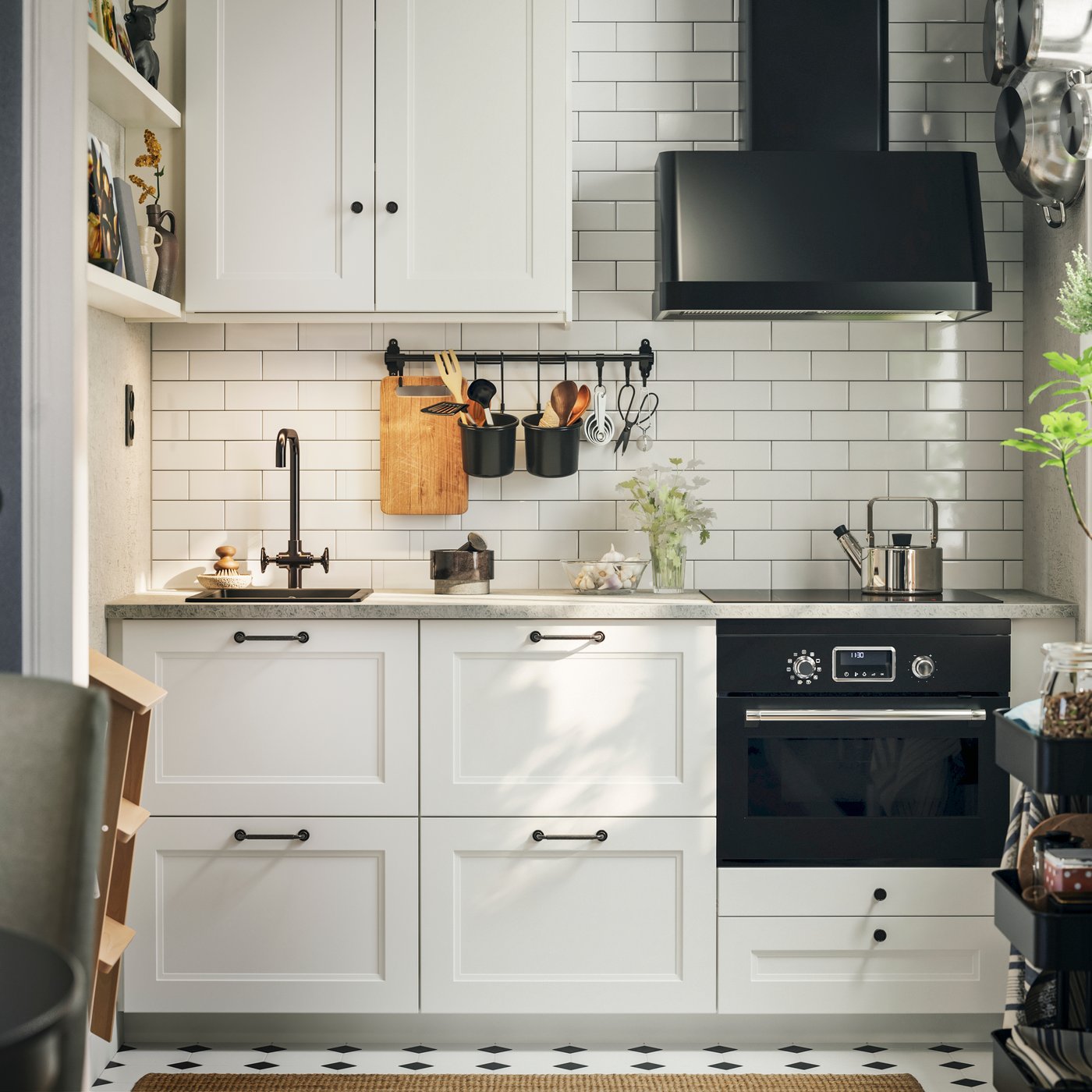 A white-tiled kitchen with matte white AXSTAD fronts and tall cabinets has black appliances and shelves on the wall.