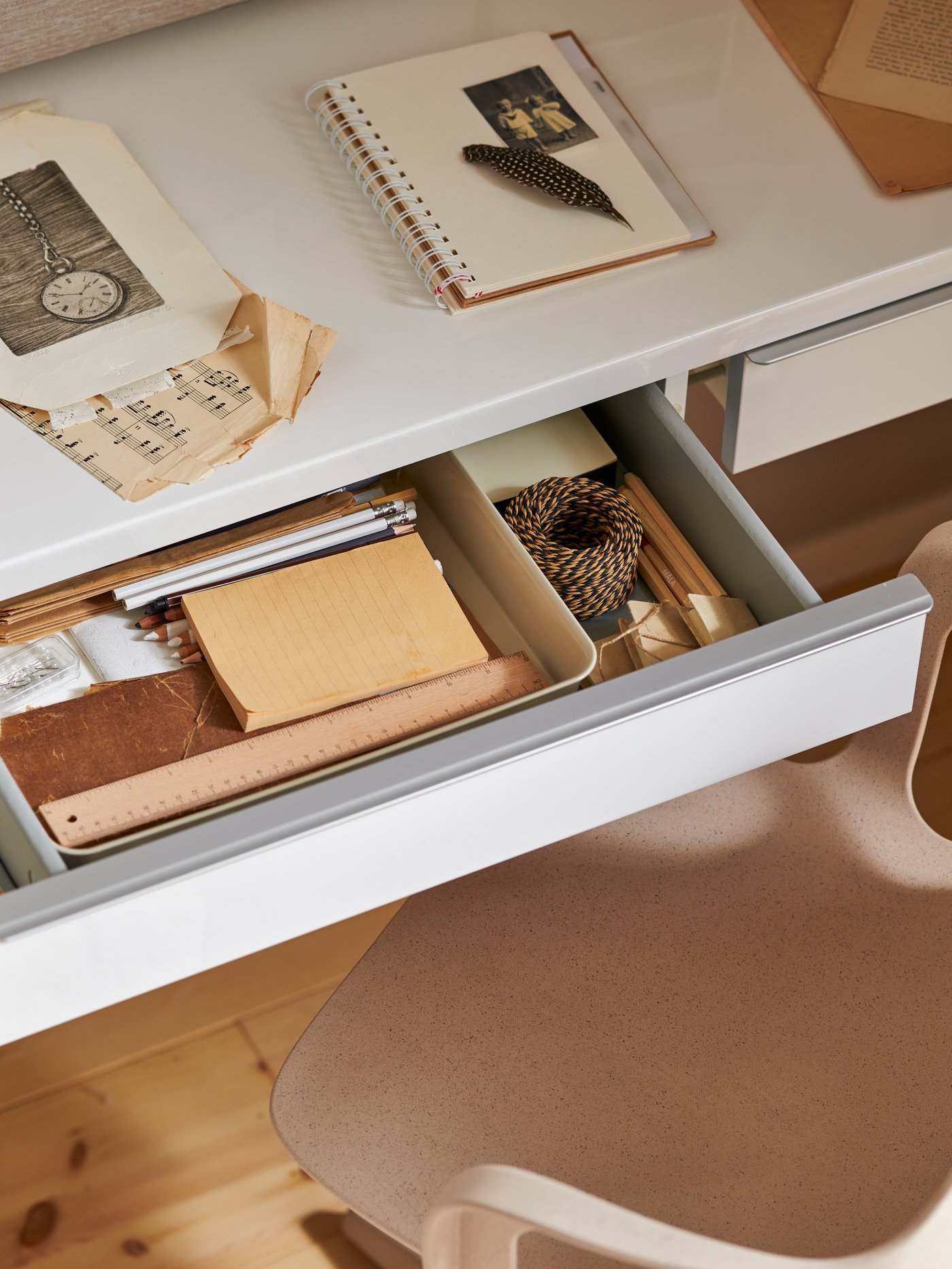 Un bureau avec un cahier posé dessus et un range-tout NOJIG en plastique beige pour bien ranger la papeterie dans le tiroir.