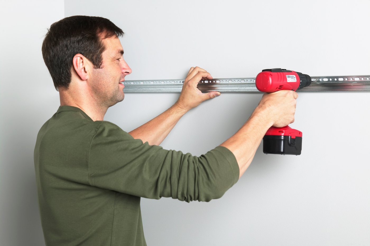 Un homme perce un rail de support d'armoire de cuisine sur un mur.