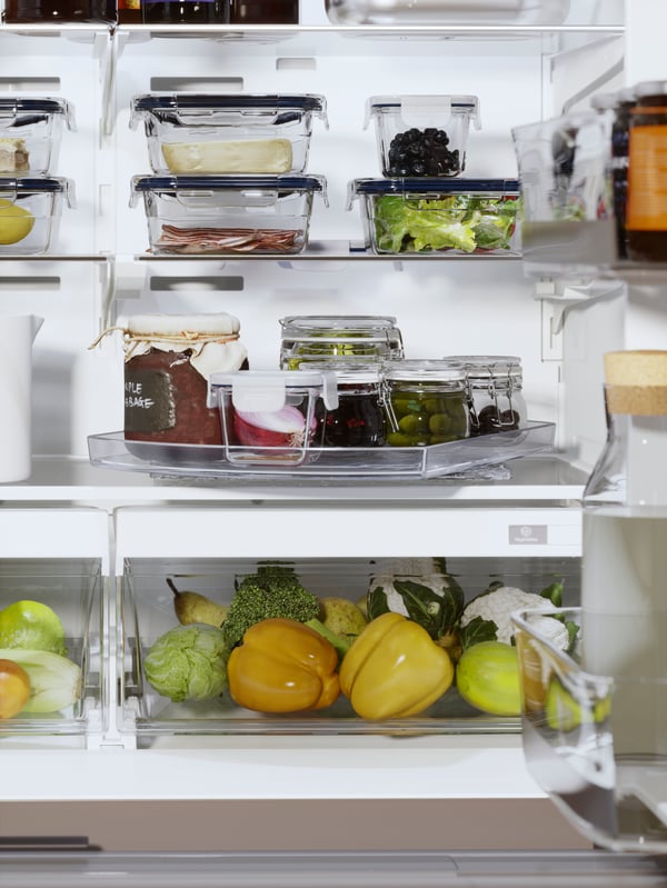 Several shelves and two drawers in a fridge holding food in containers. The lower shelf holds a SNURRAD storage turntable.