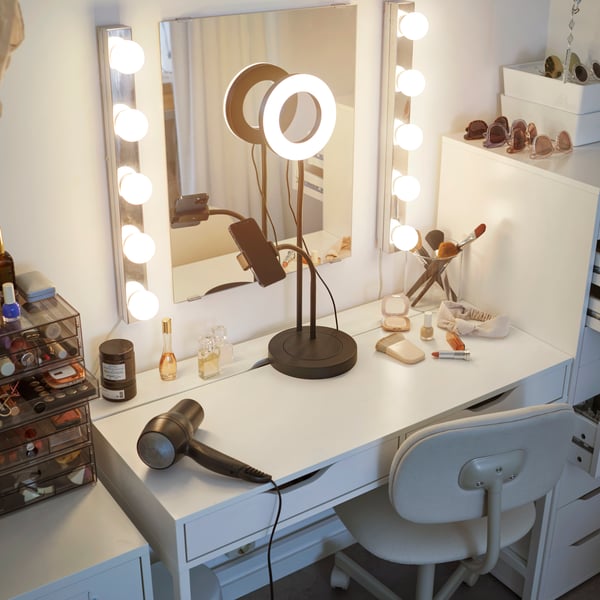 A vanity with a mirror and LEDSJÖ wall lamps on either side. A ring light is on, with hair dryer and makeup storage close by.