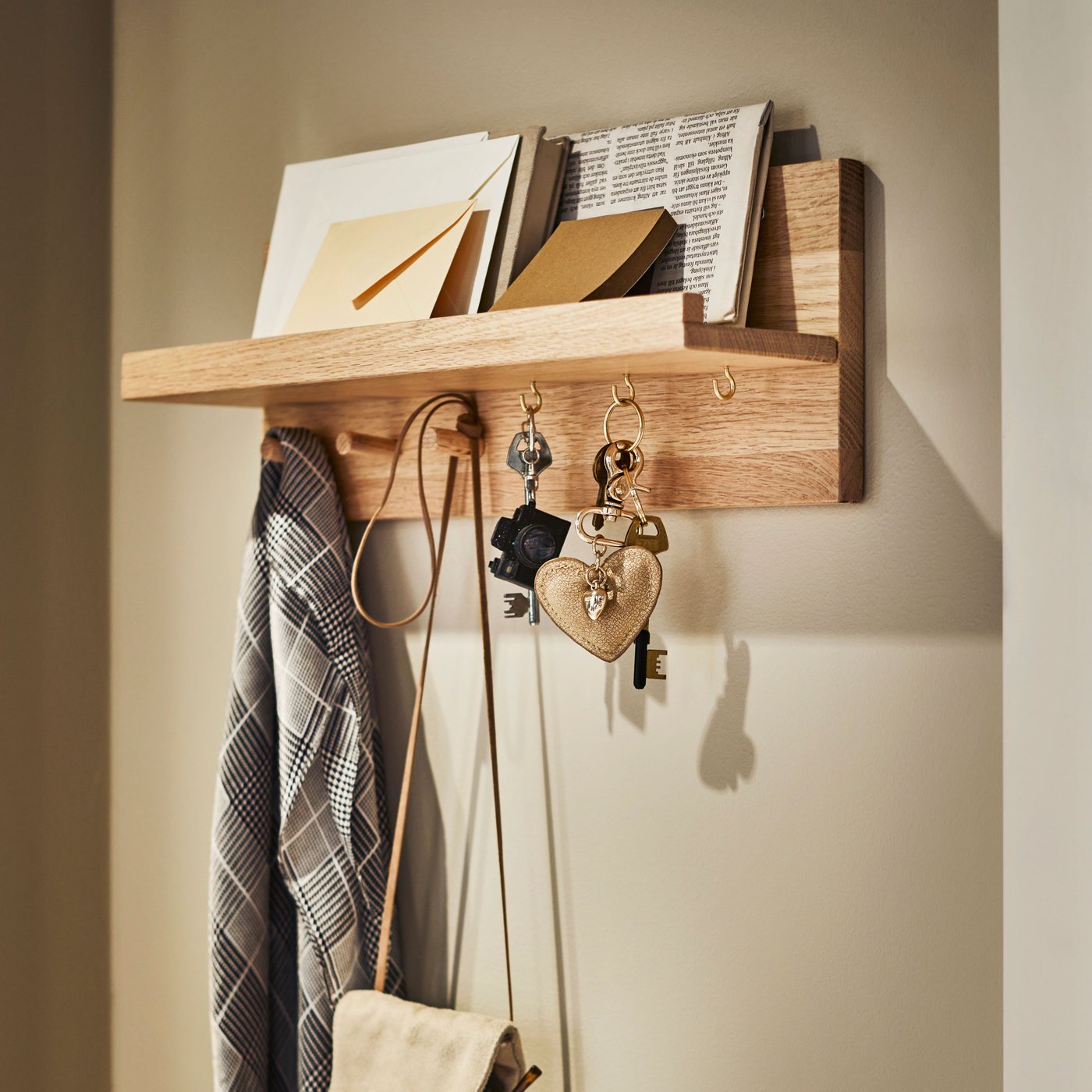 Eine HÄSTVISKARE Wandaufbewahrung mit Haken aus Eiche hängt an einer Wand. Auf ihr befinden sich Briefe und Schlüssel und an den Haken hängen eine Tasche und ein Schal.