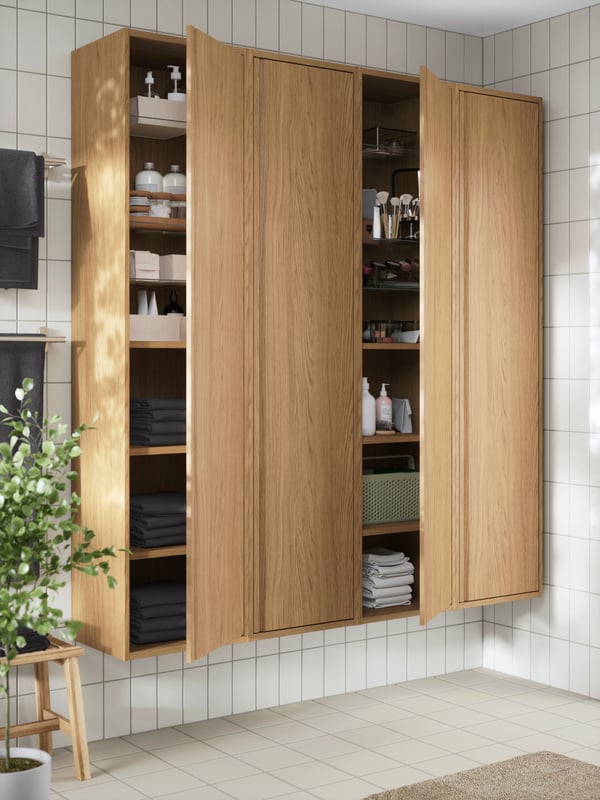 Open ÄNGSJÖN high cabinets with doors with neatly organized towels, toiletries, and bathroom essentials.