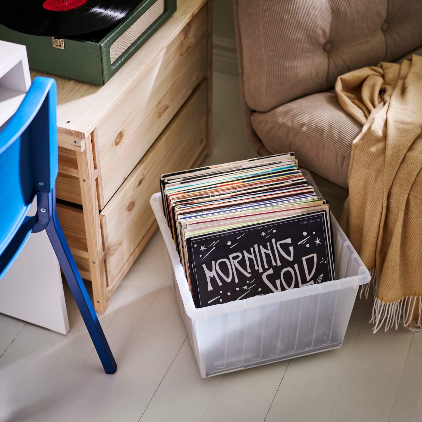 A VESSLA storage crate with castors filled with vinyl records next to a chair, desk and a KRONÖREN chest of drawers.