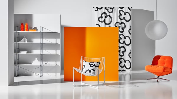 A white SKÅLBODA armchair in front of an orange screen in a room with many more products from the Nytillverkad collection.