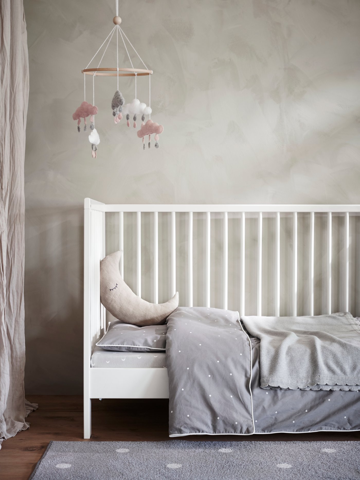 Kusyen buatan sendiri bentuk seperti bulan separa menindih bantal di atas katil bayi GULLIVER dengan satu sisi ditanggalkan dan linen katil LENAST.