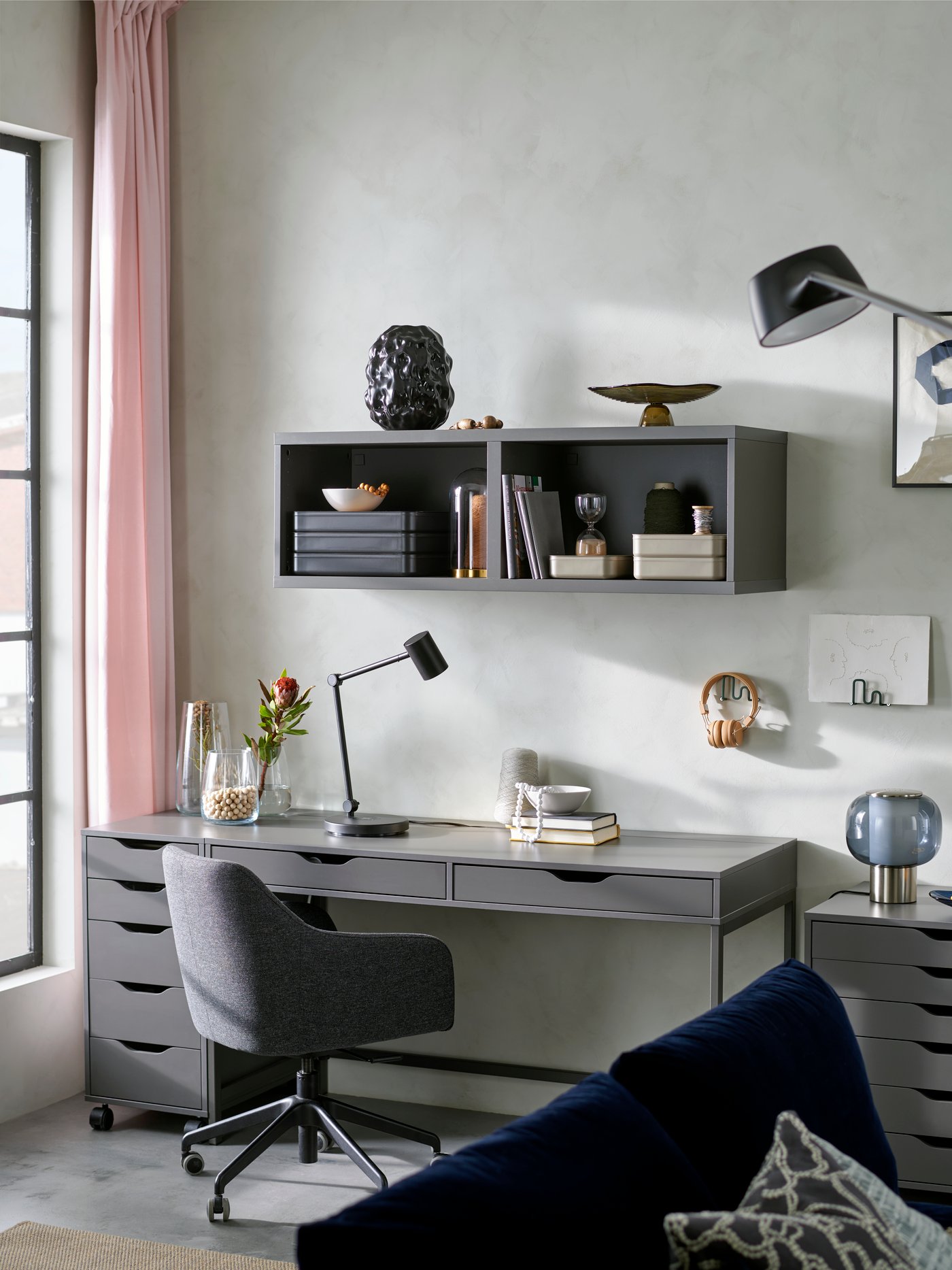 A living room workspace with a dark grey/black TOSSBERG/LÅNGFJÄLL conference chair next to an ALEX desk and storage units.