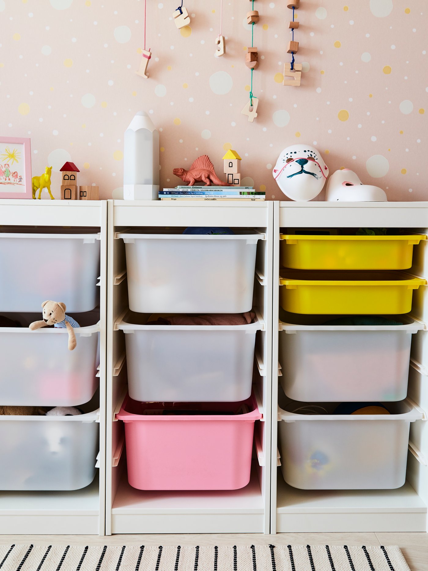 White TROFAST toy storage combination with pull-out storage trays in yellow and pink in a child's bedroom.