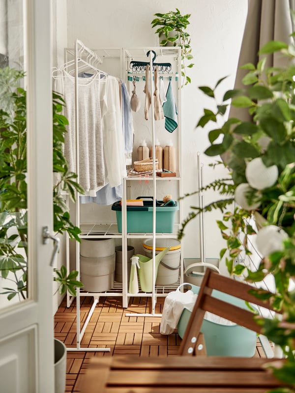 Two white MULIG clothes bars on a wall, with clothes on white hangers, beside a folding hook holding various items.