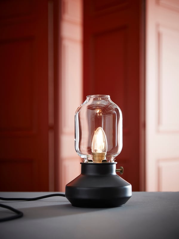 Lampu meja TÄRNABY terletak di atas permukaan berwarna kelabu di tengah-tengah ruang besar yang mempunyai dinding berpanel berwarna merah jambu.