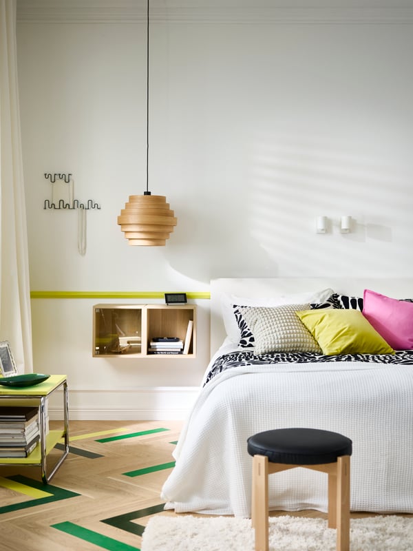 Bedroom with a double bed with black/white bedding and colourful cushions, bright colours painted on parquet floor.