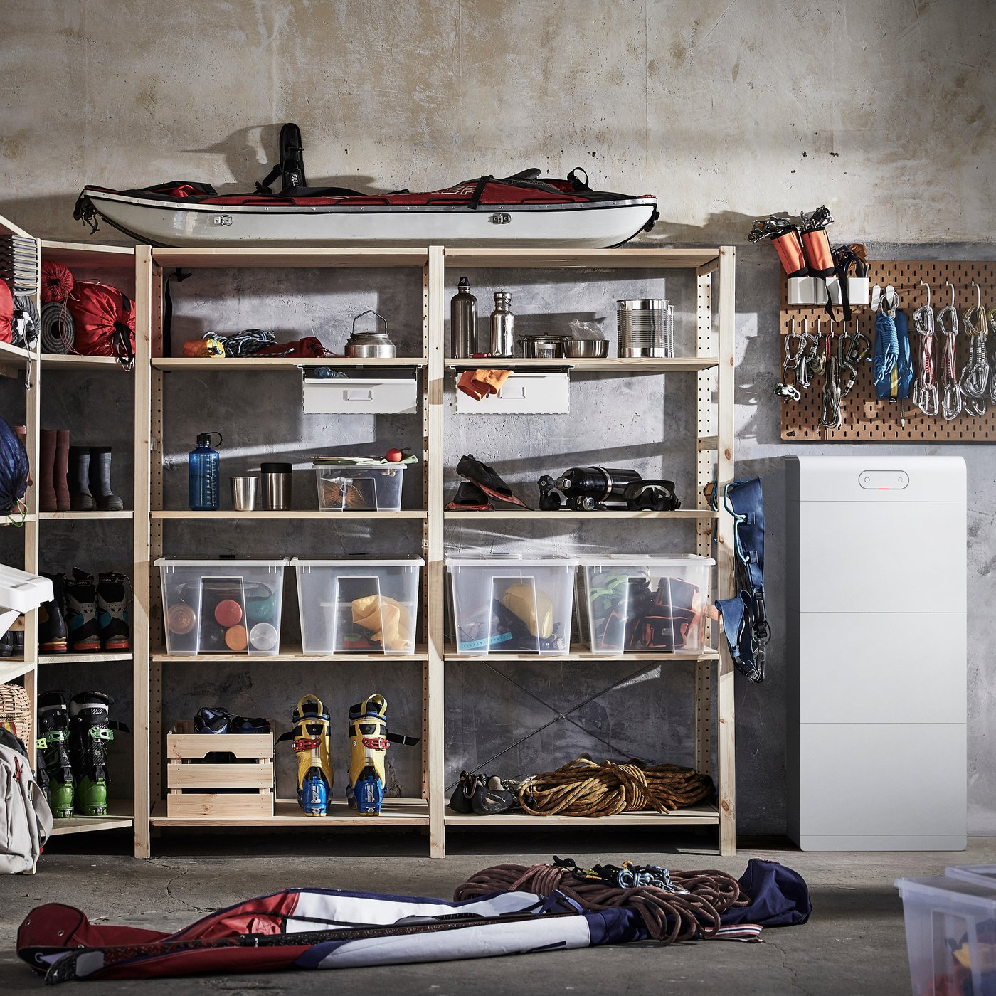 Rangement de garage organisé avec des étagères, du matériel de sport et d'extérieur, des boîtes de rangement vides et une armoire blanche posée contre un mur en béton.
