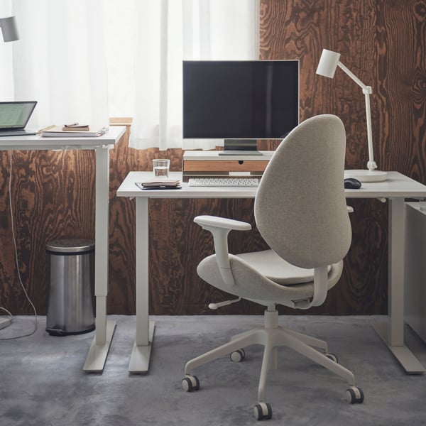 A white TROTTEN sit/stand desk with a beige HATTEFJÄLL office chair in front and a top unit with desktop computer on top.