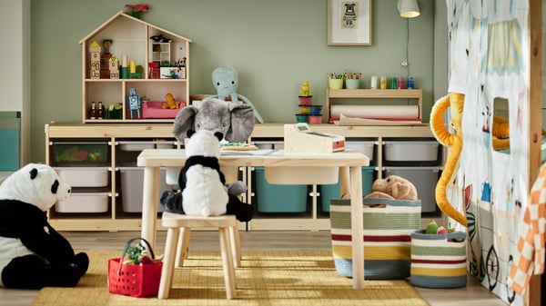 Una habitación infantil con mesas y sillas pequeñas de madera en las que hay peluches y juguetes.