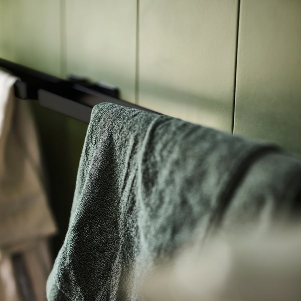 A dark green/mélange HIMLEÅN bath towel on a black SKOGSVIKEN towel rail against a green tiled wall.