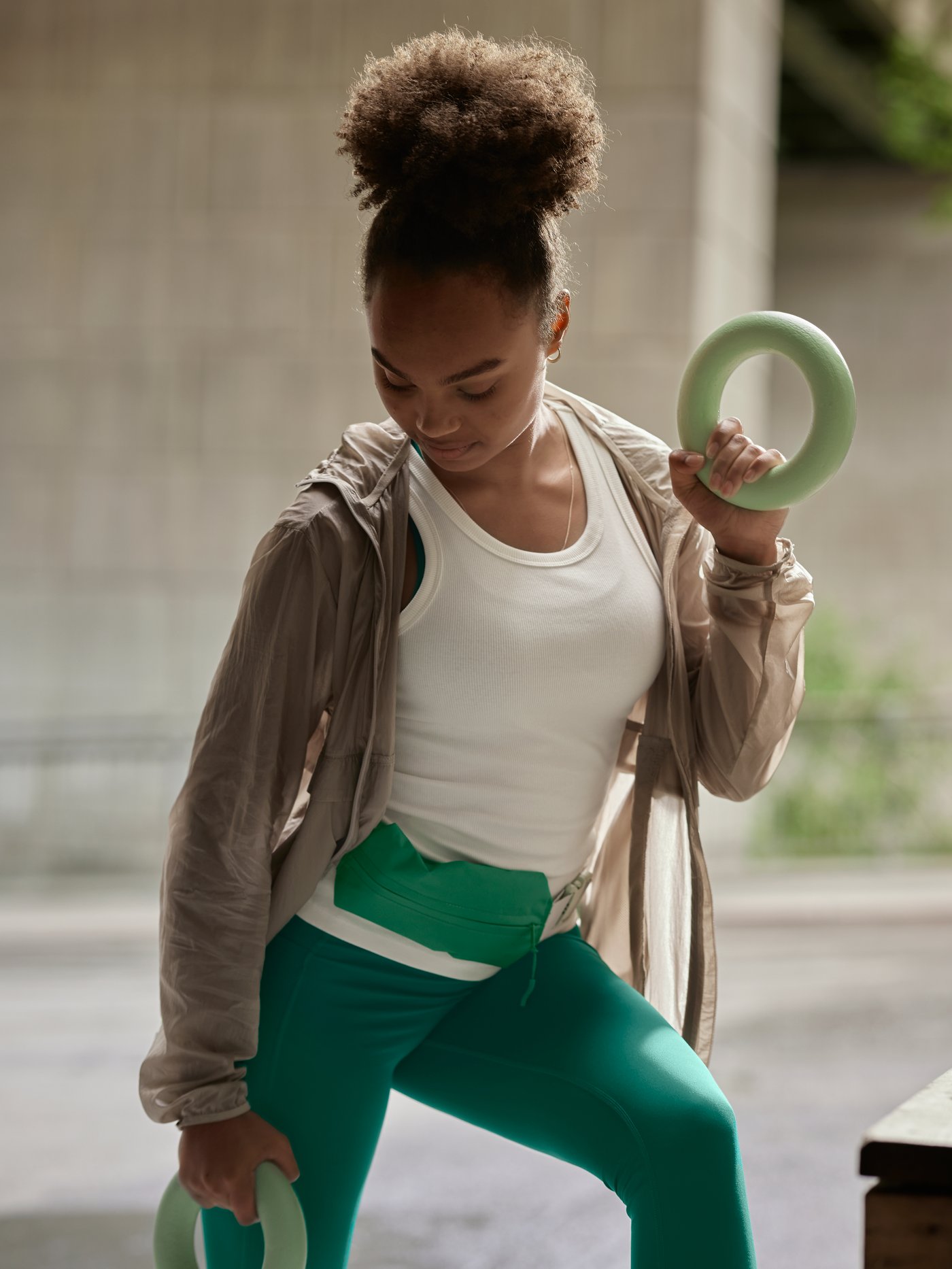 A girl wearing green leggings and the DAJLIEN belt bag holds a set of round DAJLIEN training weights in her hands.