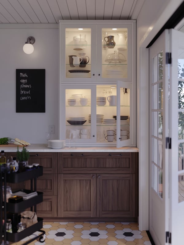 Two SEKTION cabinets with white ENKÖPING glass doors on top of a kitchen countertop filled with dinner- and serveware.