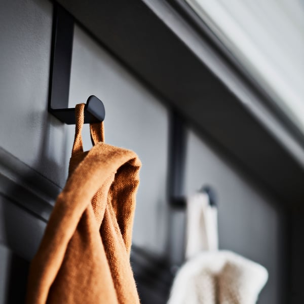 Two bathrobes, one light brown and one white, are hanging from SKOGSVIKEN hooks that are attached to the top of a dark door.