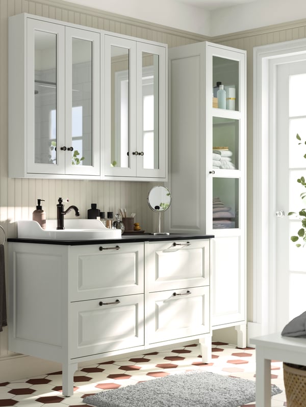 A bathroom with white and brown tiles on the floor featuring two TÄNNFORSEN wash-stands with drawers and a black countertop.
