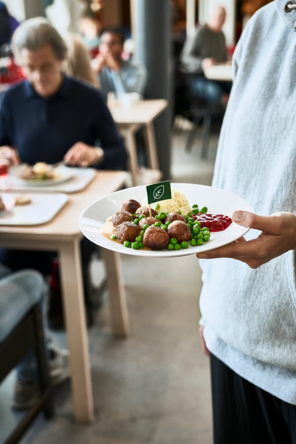 Une personne portant une chemise blanche traverse le Restaurant suédois en tenant un plat de boulettes de viande.
