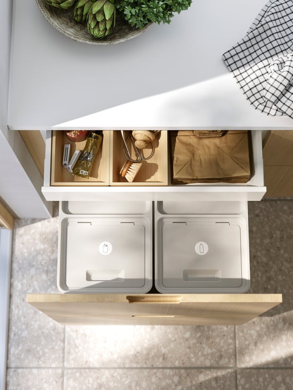 A kitchen drawer, with a FRÖJERED front, is open and contains HÅLLBAR waste bins, paper bags, brushes and sealing clips.