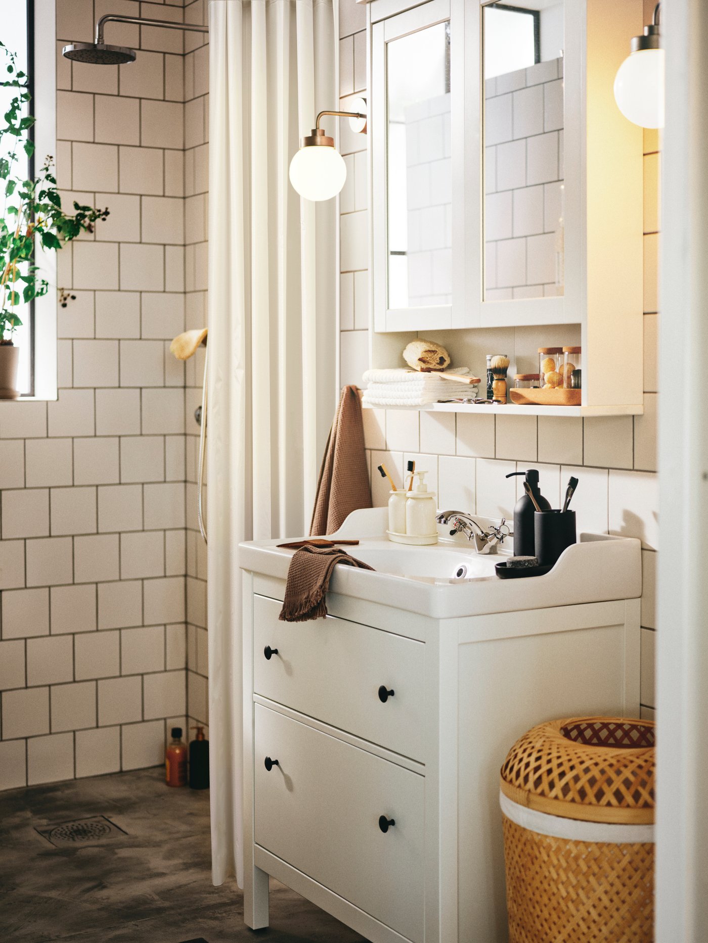 A bathroom with a HEMNES/RÄTTVIKEN wash-stand with 2 drawers below a mirror cabinet and two FRIHULT wall lamps.