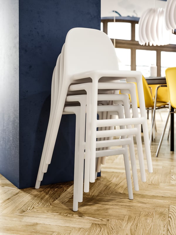 Stacked white junior chairs against a blue wall, wooden floor, white pendant lamps, and dark yellow chairs in the background.