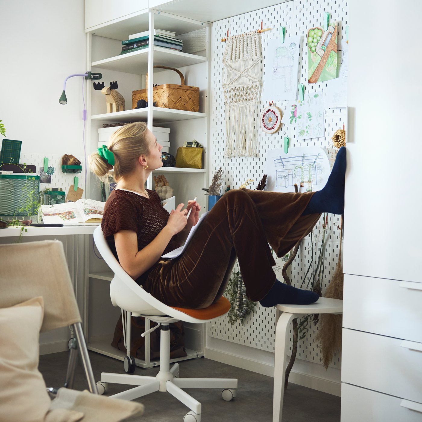A person in a desk chair looking at a wall with SKÅDIS pegboards used with accessories holding sketches and study essentials.