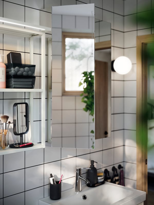 A shallow and minimalistic LETTAN mirror cabinet shown above a bathroom sink. White open wall shelves hanging next to it.