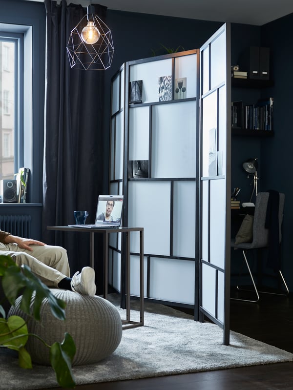A living room divided by a RISÖR room divider, with a VITTSJÖ laptop stand on one side, a compact workspace on the other.