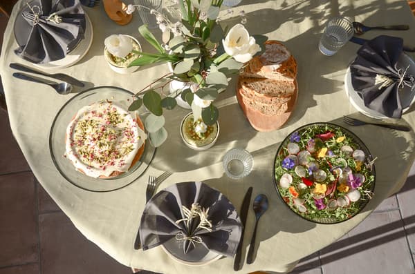 Table dressée avec fleurs, dessert, salade aux fleurs comestibles, pain et verres d’eau sur nappe claire.
