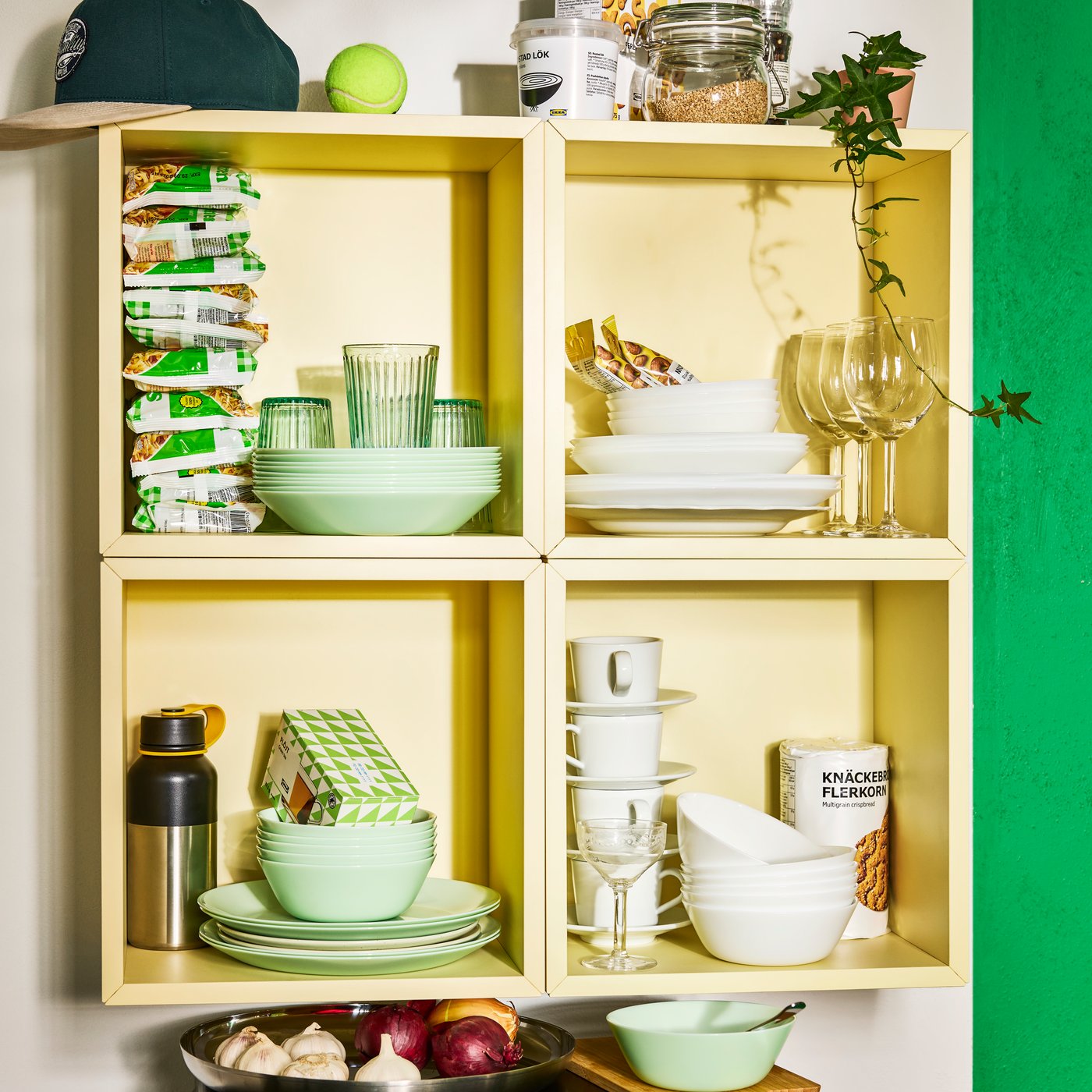 Stacks of light green and white OFTAST dinnerware on yellow shelves in student accommodation.