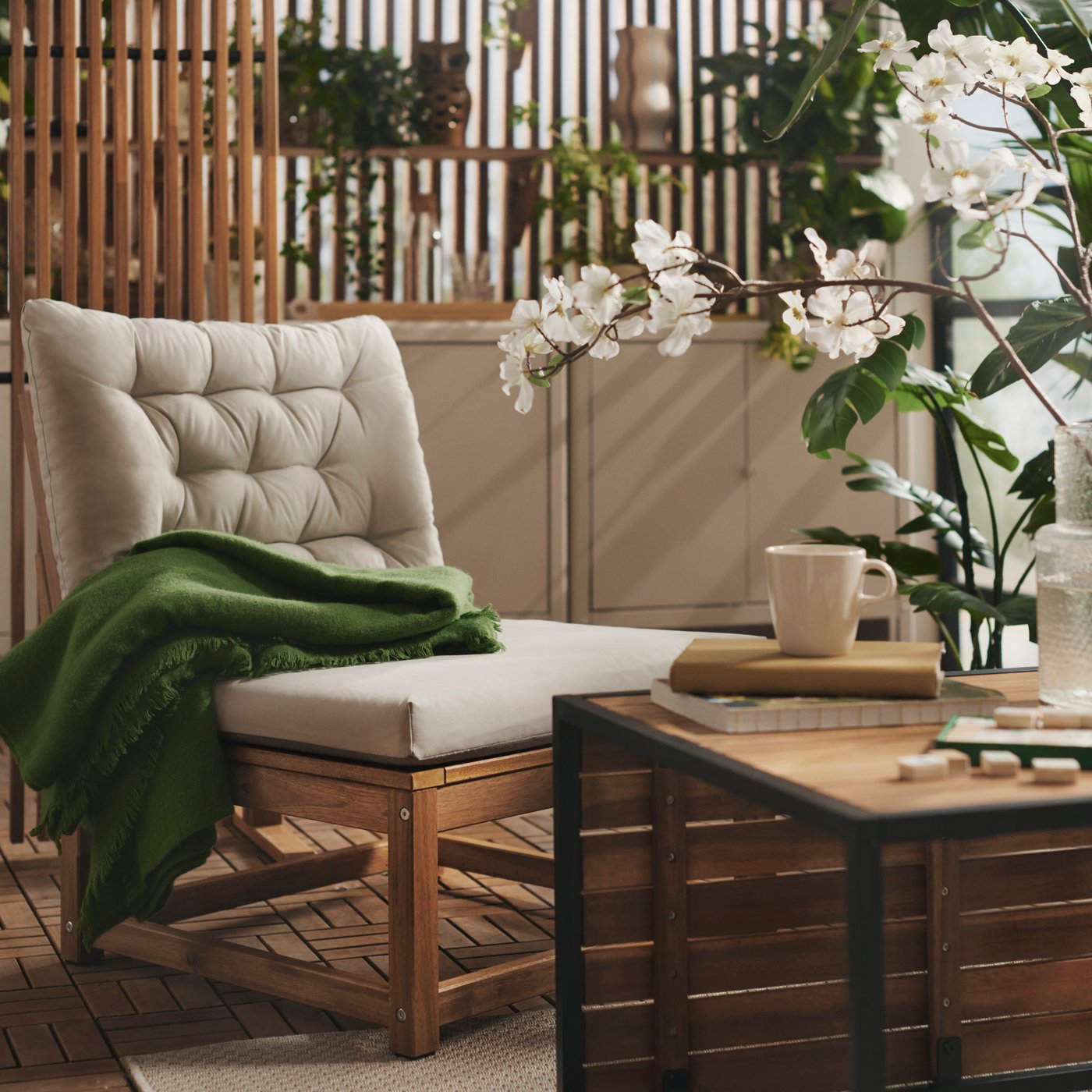 A balcony with greenery features a light brown stained NÄMMARÖ easy chair with light grey-beige cushions and a wooden table.